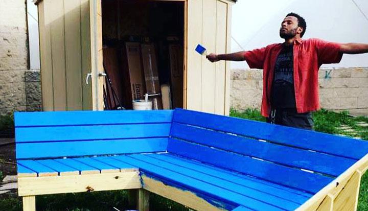 Man celebrating with arms outstretched after painting a bench